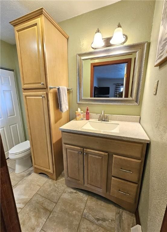 bathroom with toilet, a textured wall, and vanity