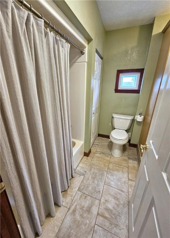 full bath featuring a textured ceiling, shower / bathtub combination with curtain, toilet, and baseboards