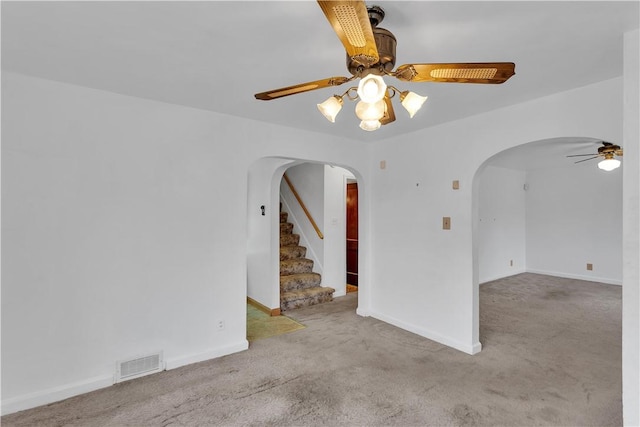 carpeted empty room with ceiling fan, stairs, visible vents, and arched walkways