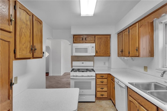 kitchen featuring white appliances, arched walkways, brown cabinets, light countertops, and a sink