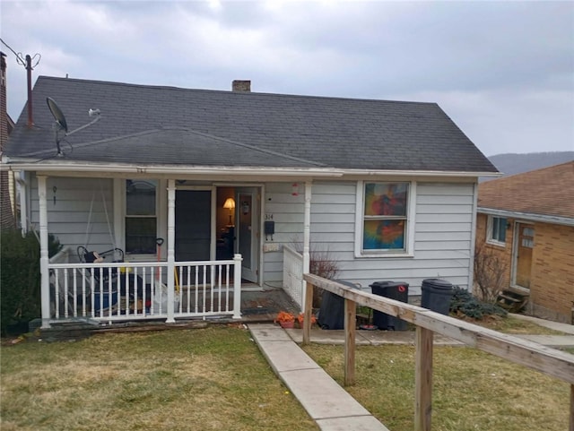 bungalow-style home featuring roof with shingles, a porch, a chimney, and a front lawn