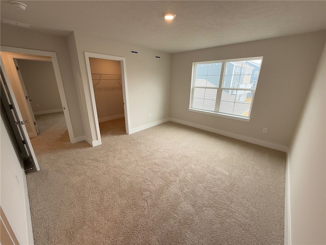 unfurnished bedroom with a walk in closet, light carpet, a textured ceiling, and baseboards