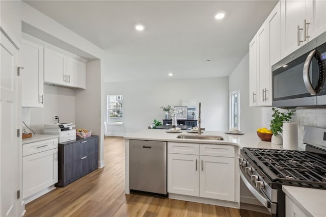 kitchen featuring stainless steel appliances, light wood-style flooring, white cabinets, a sink, and a peninsula