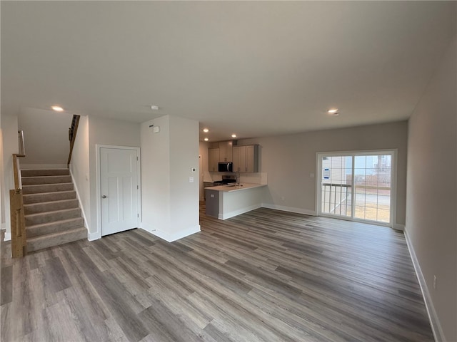 unfurnished living room with baseboards, stairway, and wood finished floors