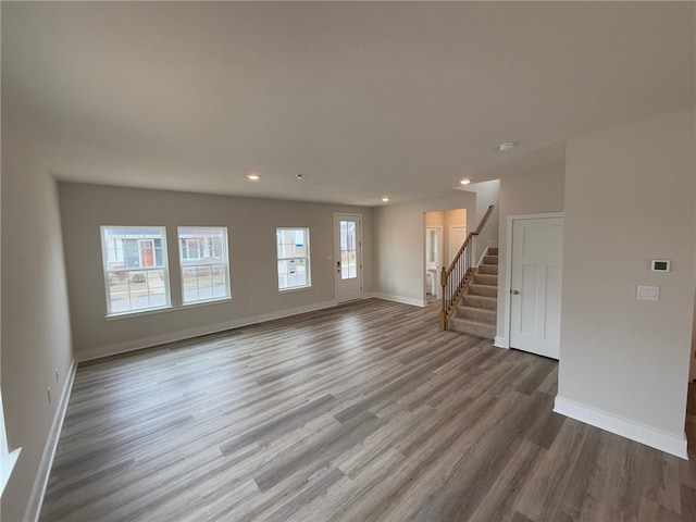 unfurnished living room featuring recessed lighting, stairway, baseboards, and wood finished floors