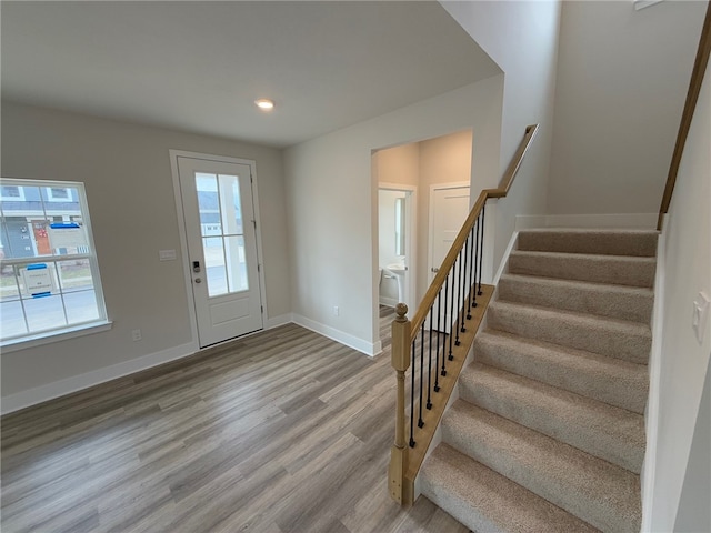 foyer entrance with a wealth of natural light, stairs, baseboards, and wood finished floors