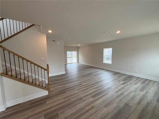 unfurnished living room featuring stairway, plenty of natural light, wood finished floors, and baseboards