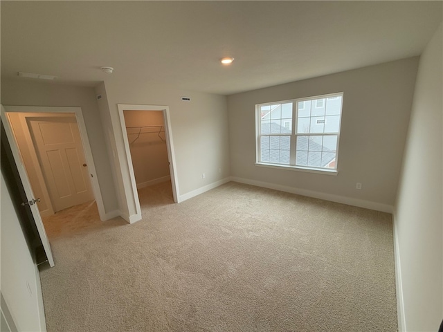 unfurnished bedroom with a walk in closet, a closet, visible vents, light carpet, and baseboards