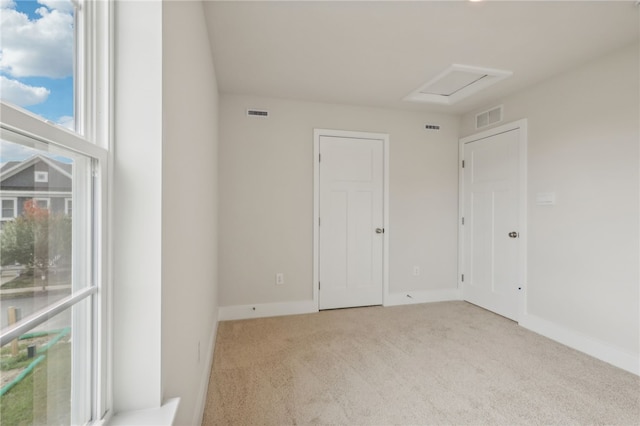 carpeted empty room with attic access, visible vents, and baseboards