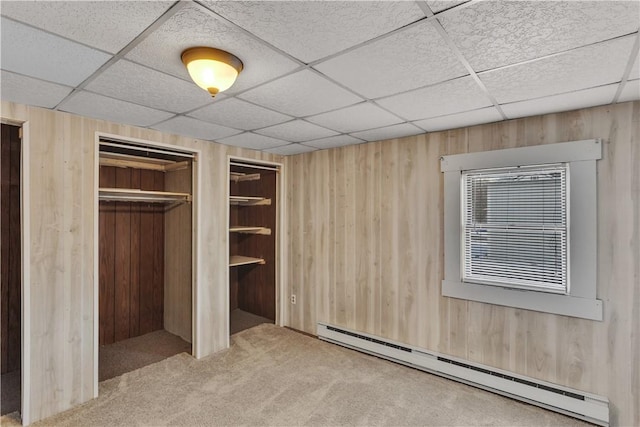 unfurnished bedroom with carpet floors, a baseboard radiator, wooden walls, and a paneled ceiling