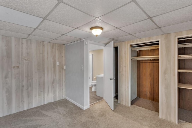 unfurnished bedroom with a closet, carpet flooring, wooden walls, and a drop ceiling