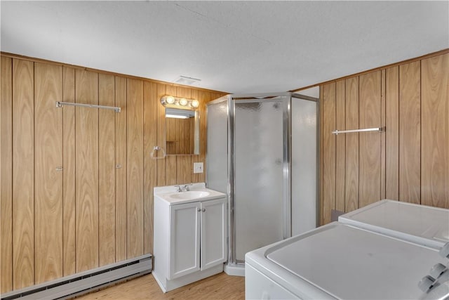 laundry room with light wood finished floors, laundry area, wooden walls, a baseboard radiator, and a sink