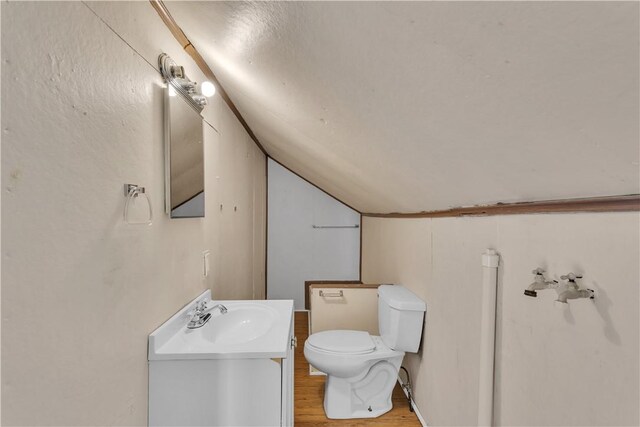 half bathroom with lofted ceiling, vanity, toilet, and wood finished floors