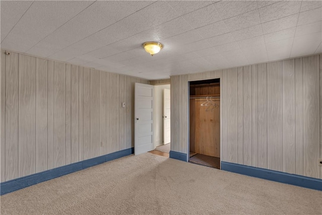 spare room featuring carpet floors, wood walls, and baseboards