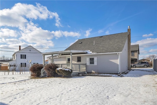 snow covered house featuring a shingled roof and a chimney