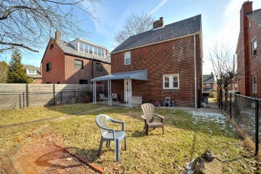 rear view of property featuring a fenced backyard, a lawn, a chimney, and brick siding