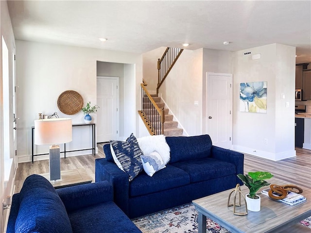 living room featuring light wood-type flooring, baseboards, and stairs