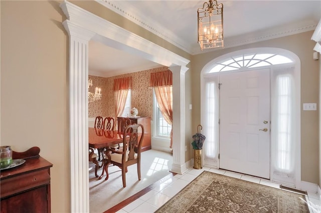 foyer with wallpapered walls, decorative columns, light tile patterned floors, ornamental molding, and a notable chandelier