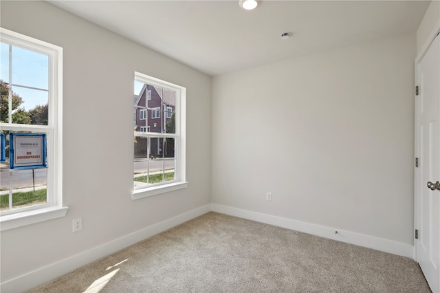 carpeted spare room featuring a healthy amount of sunlight and baseboards