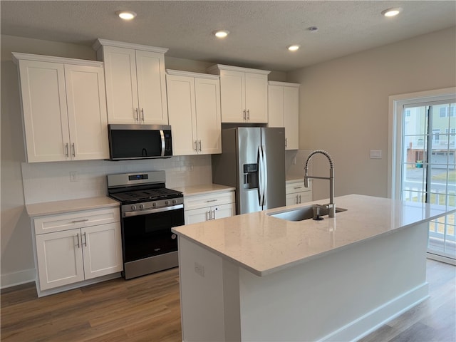 kitchen with stainless steel appliances, white cabinetry, a sink, an island with sink, and wood finished floors