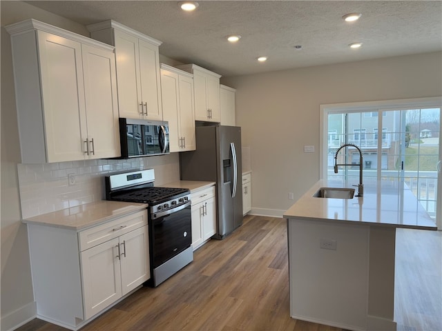 kitchen with stainless steel appliances, tasteful backsplash, light countertops, a sink, and wood finished floors