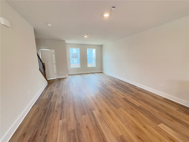 unfurnished living room featuring stairs, baseboards, and wood finished floors