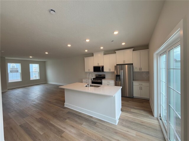 kitchen with light wood finished floors, appliances with stainless steel finishes, light countertops, white cabinetry, and a sink