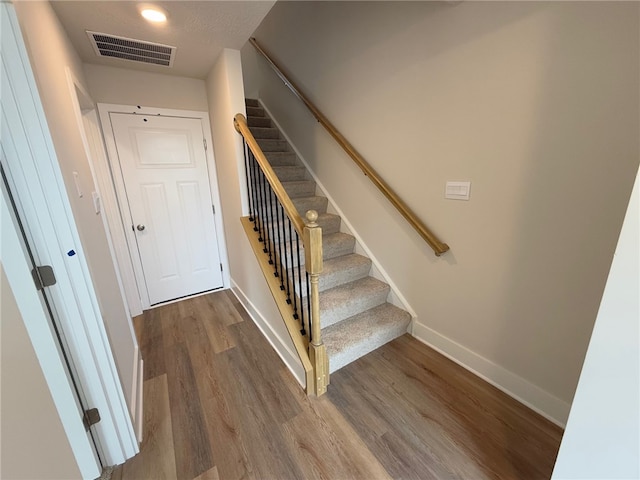 staircase with wood finished floors, visible vents, and baseboards