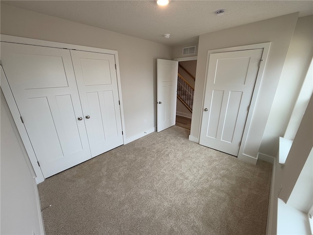 unfurnished bedroom featuring visible vents, a closet, light carpet, and a textured ceiling