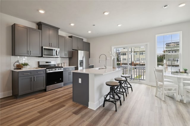 kitchen with a breakfast bar area, decorative backsplash, appliances with stainless steel finishes, light wood-style floors, and a sink