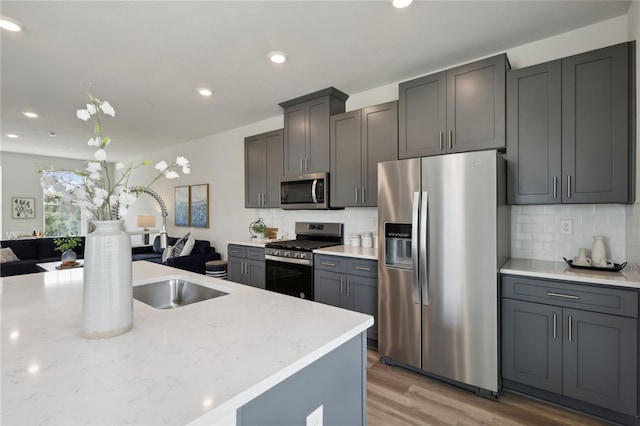 kitchen with light wood finished floors, recessed lighting, backsplash, appliances with stainless steel finishes, and open floor plan