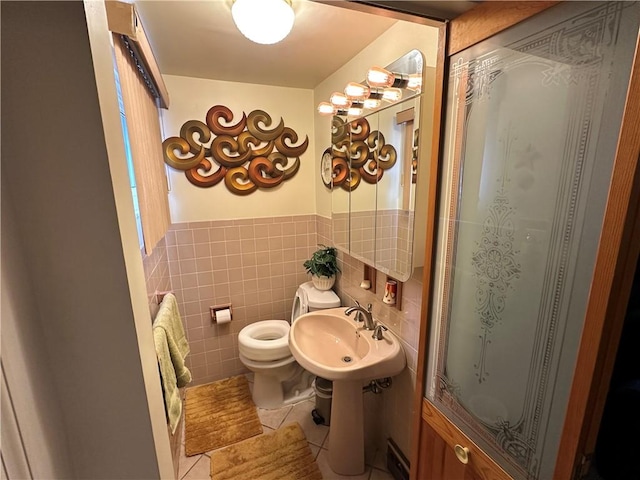 bathroom featuring tile walls, toilet, a wainscoted wall, tile patterned floors, and a sink