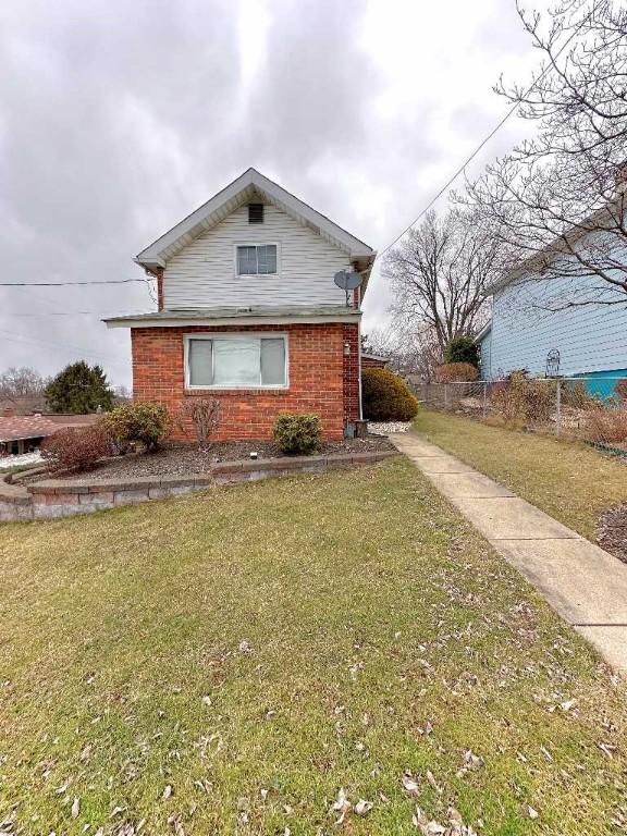 view of home's exterior featuring brick siding, a lawn, and fence