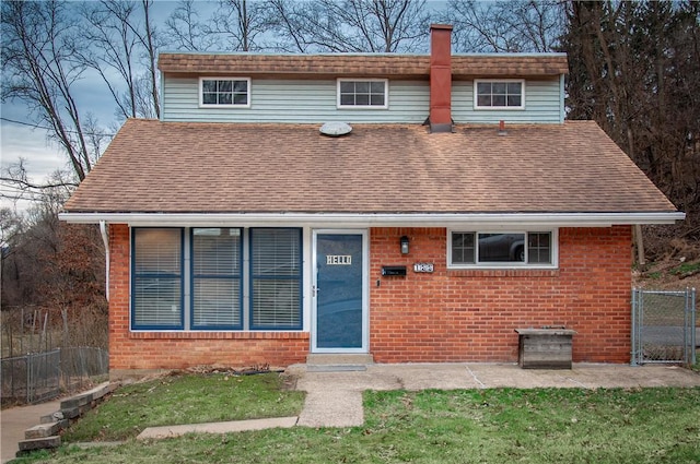 view of front of house with a gate, brick siding, fence, and roof with shingles