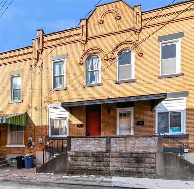 townhome / multi-family property with covered porch, brick siding, and entry steps