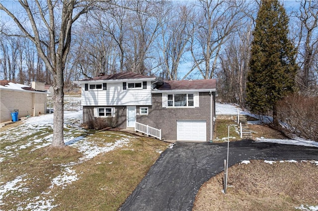 split level home featuring aphalt driveway, brick siding, a chimney, and an attached garage