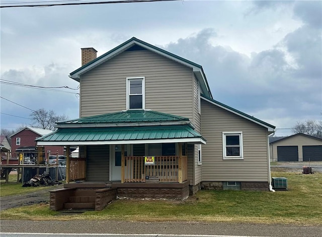 view of front facade featuring metal roof, covered porch, a detached garage, a front lawn, and a chimney