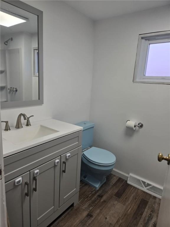 bathroom with toilet, wood finished floors, vanity, visible vents, and a shower