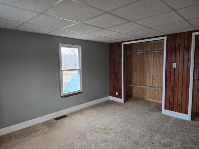 unfurnished bedroom featuring carpet, visible vents, wooden walls, and baseboards