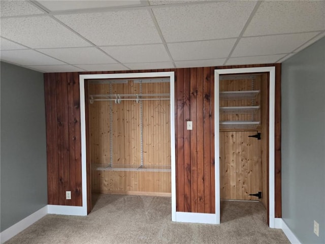 unfurnished bedroom featuring a paneled ceiling, carpet flooring, wood walls, and baseboards