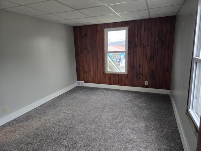 carpeted empty room featuring a paneled ceiling, visible vents, wood walls, and baseboards