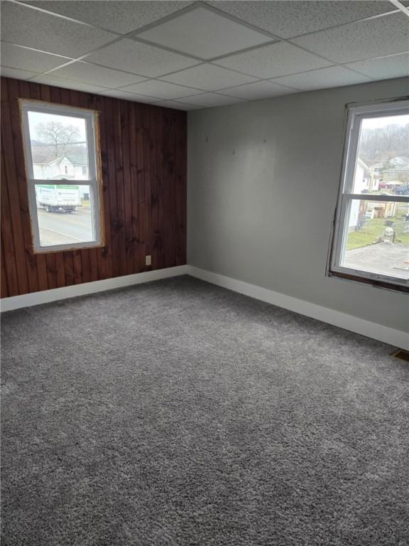 carpeted spare room featuring a drop ceiling, plenty of natural light, and baseboards