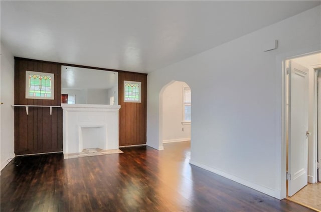 unfurnished living room featuring arched walkways, plenty of natural light, baseboards, and wood finished floors