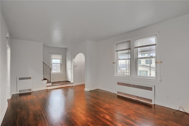 unfurnished living room featuring arched walkways, radiator heating unit, wood finished floors, and stairs