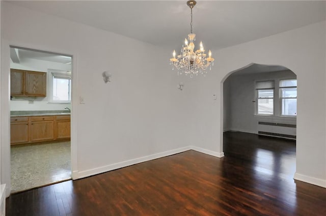 unfurnished dining area featuring arched walkways, radiator heating unit, a sink, wood finished floors, and baseboards