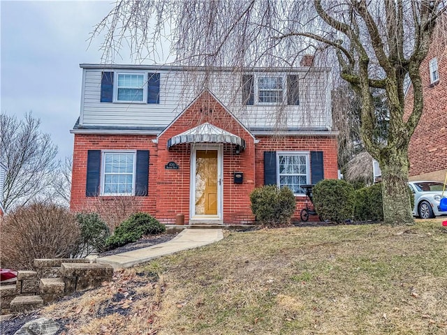 view of front of home with a front yard, brick siding, and a chimney