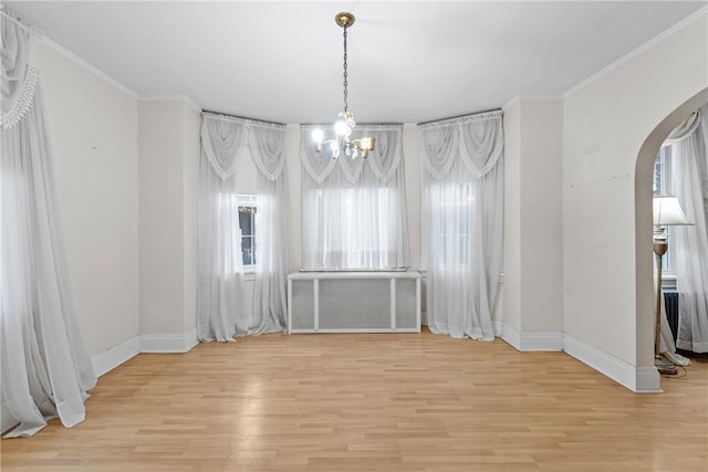 unfurnished dining area featuring light wood-style floors, arched walkways, and ornamental molding