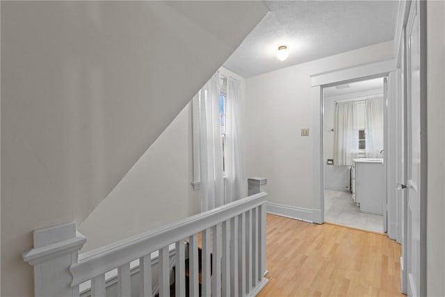 hall featuring light wood-type flooring, baseboards, plenty of natural light, and an upstairs landing