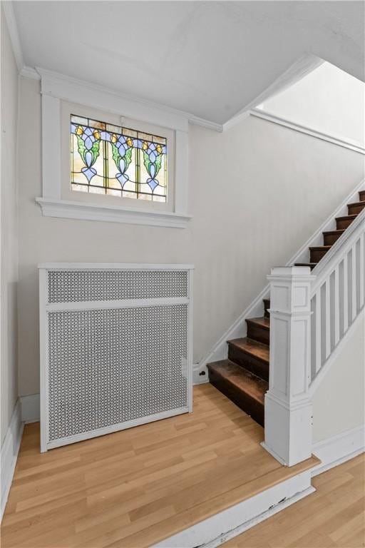 stairway featuring radiator, baseboards, wood finished floors, and ornamental molding