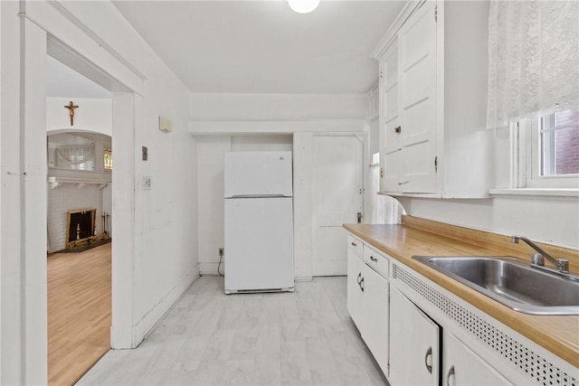 kitchen featuring a fireplace, a sink, white cabinets, light countertops, and freestanding refrigerator